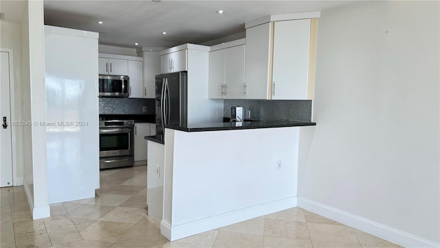 kitchen featuring light tile patterned floors, appliances with stainless steel finishes, kitchen peninsula, decorative backsplash, and white cabinets