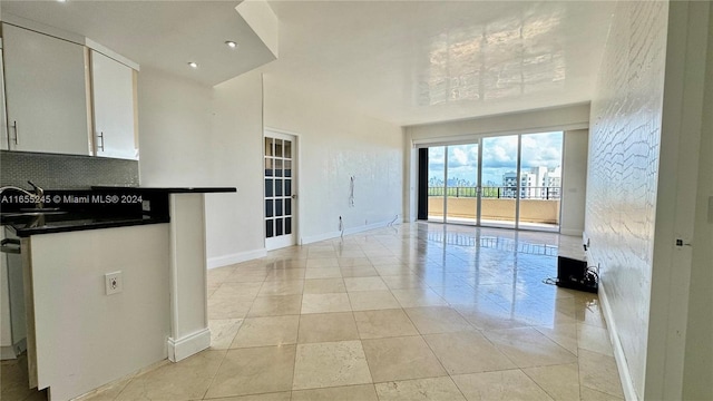 kitchen featuring tasteful backsplash, light tile patterned floors, white cabinetry, and sink