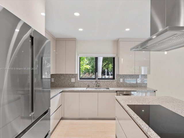 kitchen featuring light stone counters, stainless steel refrigerator, sink, wall chimney exhaust hood, and black electric stovetop