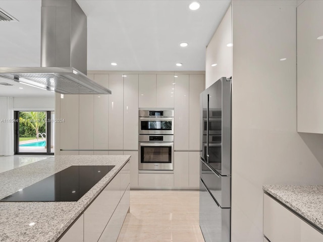 kitchen with white cabinets, light tile patterned floors, appliances with stainless steel finishes, light stone counters, and island exhaust hood