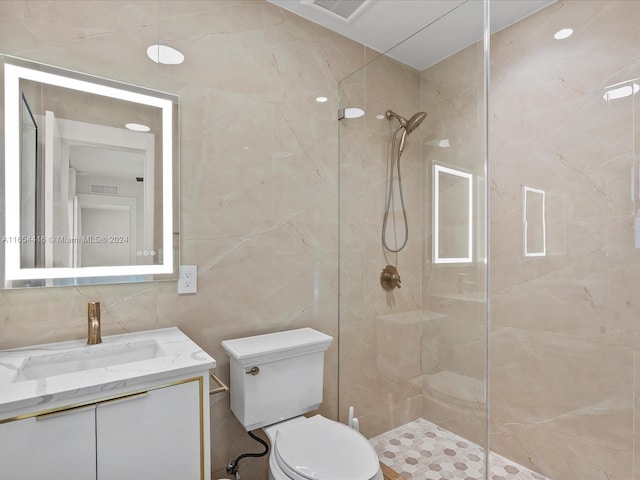 bathroom with vanity, toilet, a tile shower, and tile walls