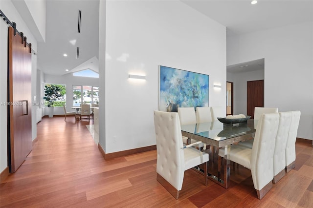 dining room with a barn door, light hardwood / wood-style floors, and high vaulted ceiling