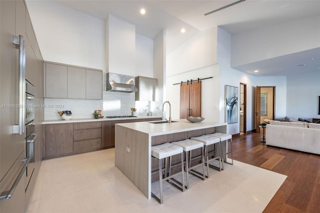 kitchen with a barn door, high vaulted ceiling, light hardwood / wood-style floors, a kitchen bar, and a kitchen island with sink