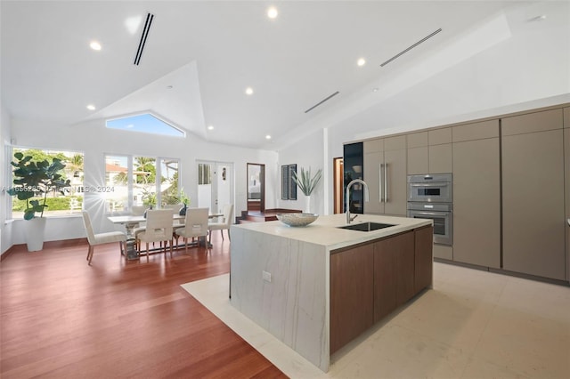 kitchen featuring a kitchen island with sink, double oven, sink, high vaulted ceiling, and light hardwood / wood-style floors