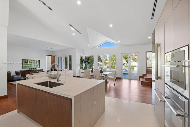 kitchen featuring light wood-type flooring, a kitchen island with sink, sink, high vaulted ceiling, and white cabinets