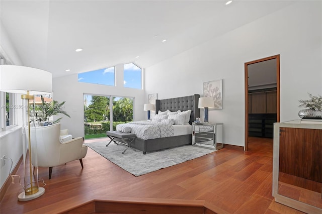 bedroom with a walk in closet, a closet, high vaulted ceiling, and hardwood / wood-style flooring