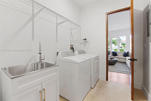 clothes washing area with cabinets, light wood-type flooring, washing machine and dryer, and sink