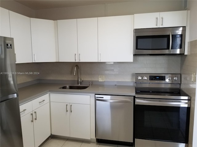 kitchen with appliances with stainless steel finishes, light tile patterned floors, sink, and white cabinets