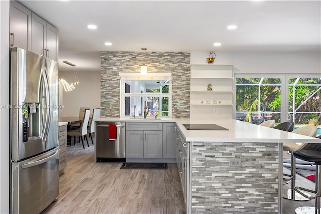 kitchen featuring gray cabinetry, a kitchen breakfast bar, hanging light fixtures, kitchen peninsula, and stainless steel appliances