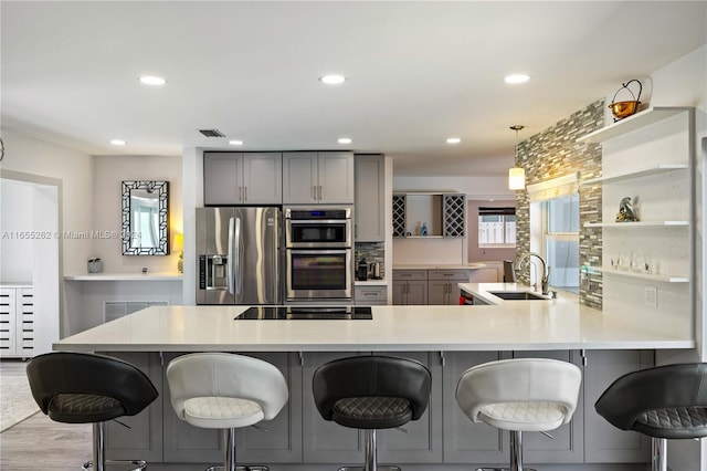 kitchen with gray cabinetry, sink, stainless steel appliances, a kitchen breakfast bar, and kitchen peninsula