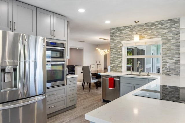 kitchen with sink, light hardwood / wood-style flooring, decorative light fixtures, decorative backsplash, and appliances with stainless steel finishes