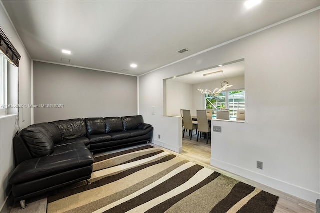 living room with light wood-type flooring, crown molding, and an inviting chandelier