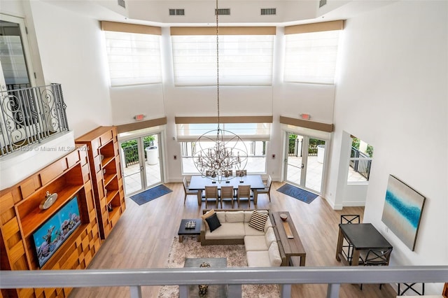 living room with a towering ceiling, wood-type flooring, a notable chandelier, and french doors