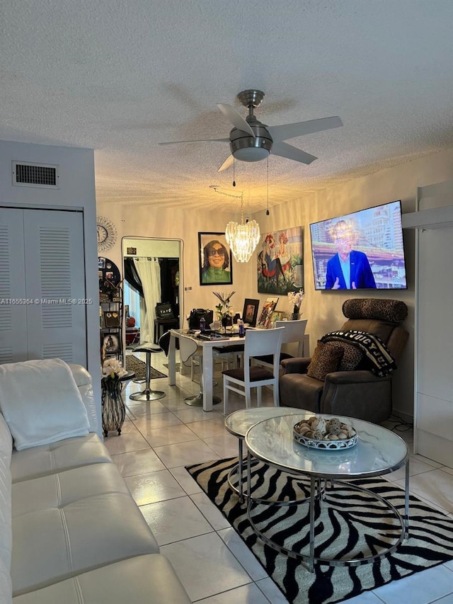 living room with ceiling fan with notable chandelier, light tile patterned flooring, and a textured ceiling