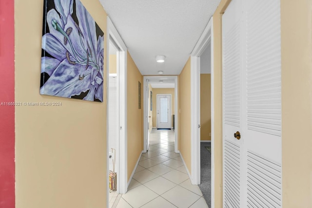 hallway with a textured ceiling and light tile patterned floors