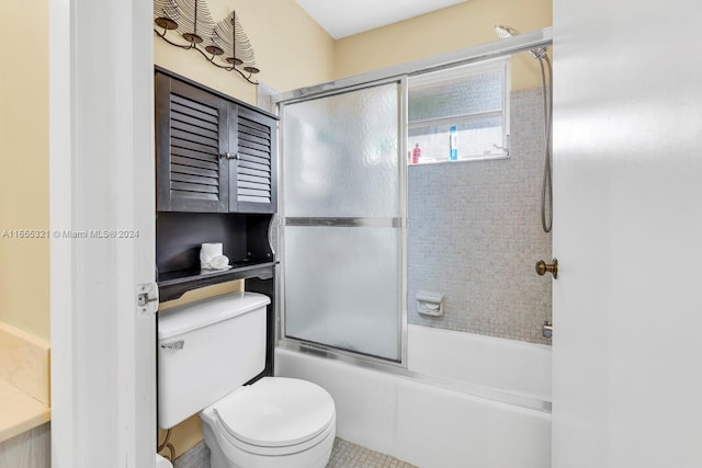 bathroom with tile patterned flooring, shower / bath combination with glass door, and toilet