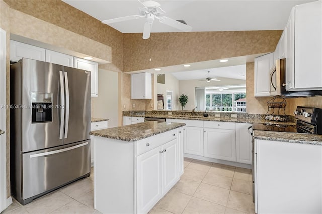 kitchen featuring stainless steel appliances, white cabinetry, vaulted ceiling, and dark stone countertops