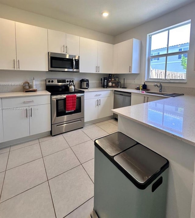 kitchen featuring light tile patterned floors, appliances with stainless steel finishes, sink, white cabinetry, and light stone counters