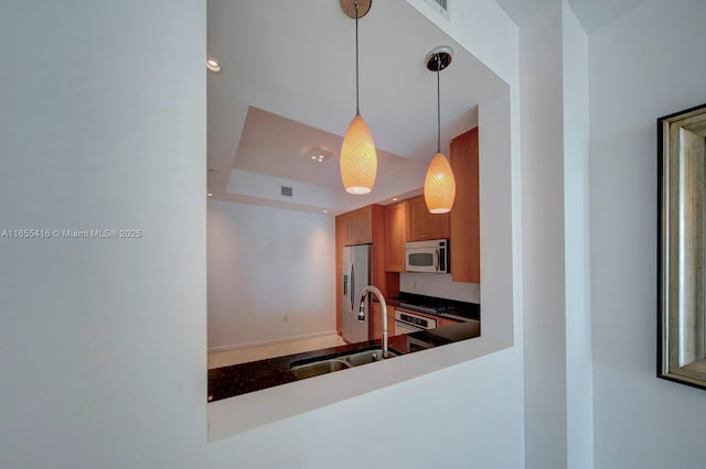 kitchen with a tray ceiling, sink, stainless steel appliances, and decorative light fixtures