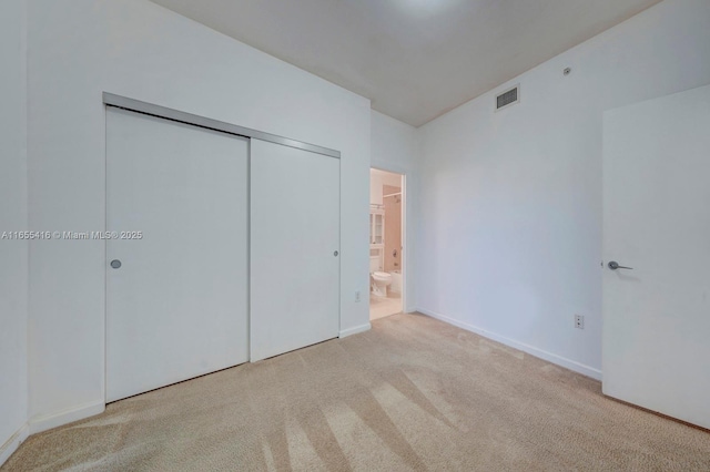 unfurnished bedroom featuring light carpet, connected bathroom, and a closet