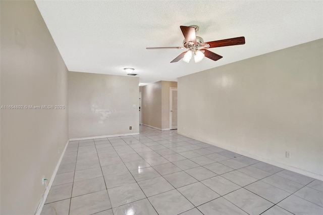 empty room with a ceiling fan, light tile patterned floors, baseboards, and a textured ceiling