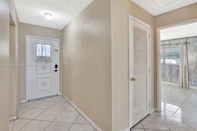 doorway featuring baseboards, light tile patterned floors, and a textured ceiling