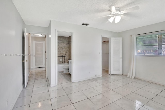 unfurnished bedroom featuring light tile patterned floors, baseboards, a walk in closet, a textured ceiling, and ceiling fan