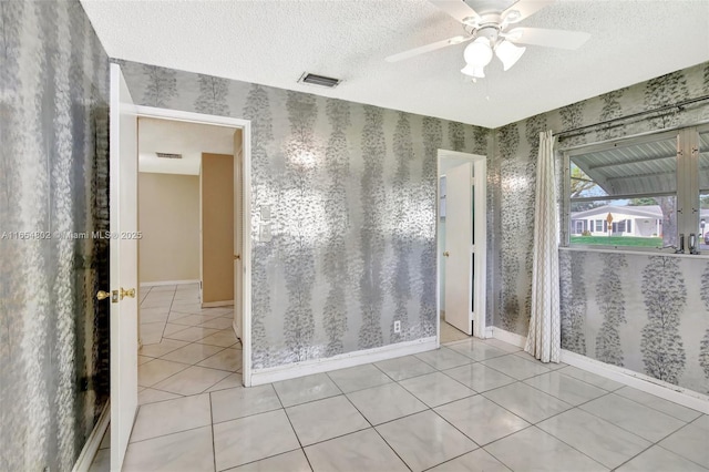 spare room with wallpapered walls, a textured ceiling, light tile patterned floors, ceiling fan, and baseboards