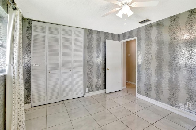 unfurnished bedroom featuring wallpapered walls, tile patterned floors, a closet, baseboards, and a ceiling fan