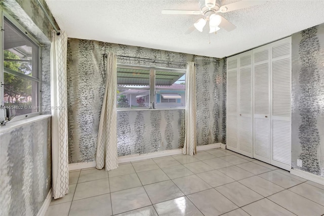 unfurnished bedroom featuring wallpapered walls, a textured ceiling, baseboards, tile patterned flooring, and a ceiling fan