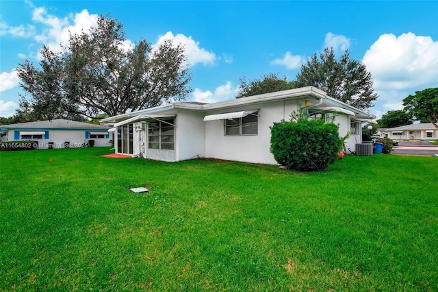 rear view of house featuring stucco siding, central AC, and a yard