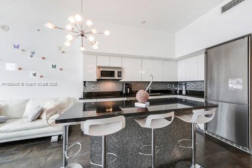 kitchen with white cabinetry, an inviting chandelier, a center island, a breakfast bar, and appliances with stainless steel finishes