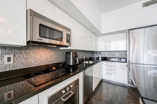 kitchen with decorative backsplash, white cabinetry, appliances with stainless steel finishes, dark stone countertops, and sink