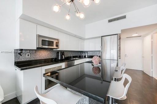 kitchen featuring stainless steel appliances, a notable chandelier, white cabinets, and decorative backsplash