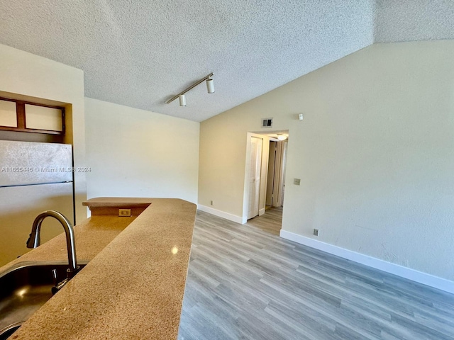 kitchen featuring hardwood / wood-style floors, a textured ceiling, vaulted ceiling, fridge, and sink