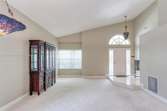 foyer with high vaulted ceiling, light colored carpet, and plenty of natural light