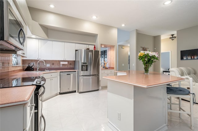 kitchen with stainless steel appliances, a center island, white cabinets, backsplash, and a breakfast bar