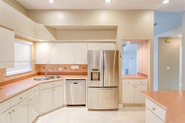 kitchen featuring sink, light tile patterned flooring, backsplash, white cabinetry, and appliances with stainless steel finishes