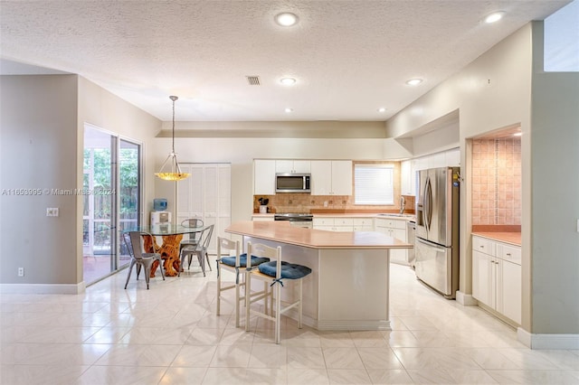 kitchen featuring tasteful backsplash, a kitchen island, appliances with stainless steel finishes, pendant lighting, and white cabinets