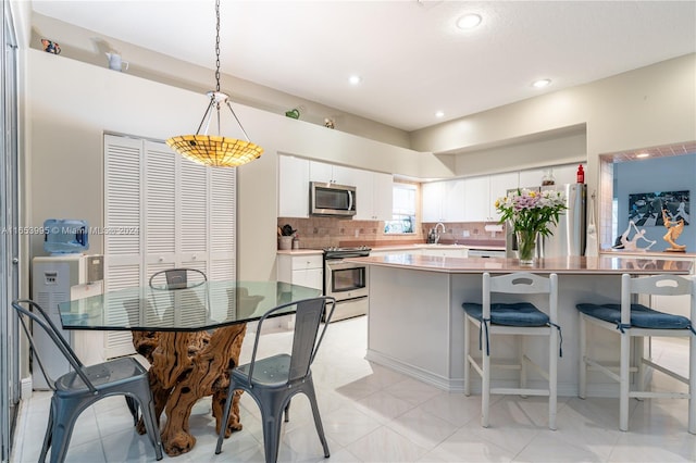 kitchen featuring white cabinetry, appliances with stainless steel finishes, light tile patterned floors, pendant lighting, and decorative backsplash