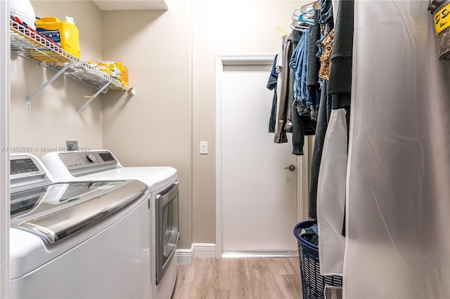 clothes washing area with washer and clothes dryer and light wood-type flooring