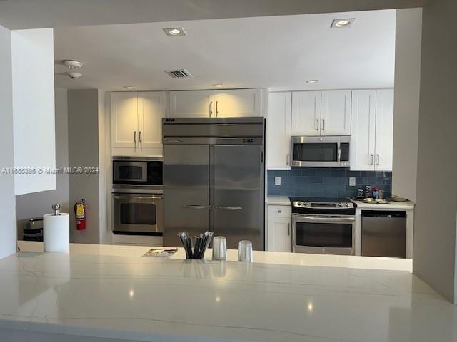 kitchen featuring built in appliances, light stone countertops, backsplash, and white cabinetry