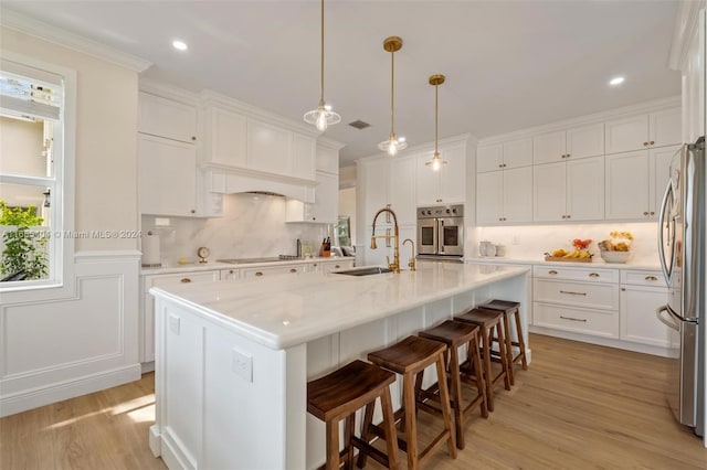 kitchen with white cabinetry, sink, stainless steel appliances, an island with sink, and light wood-type flooring