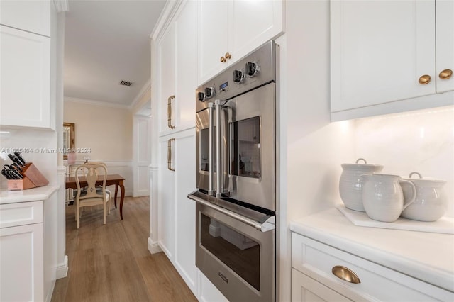 kitchen featuring white cabinets, stainless steel double oven, crown molding, and light hardwood / wood-style flooring