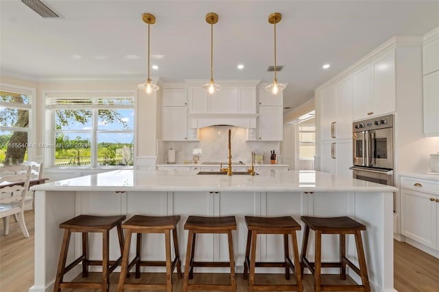 kitchen featuring light hardwood / wood-style floors, white cabinetry, hanging light fixtures, and a large island with sink