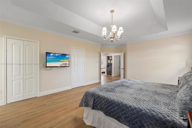 bedroom with ornamental molding, wood-type flooring, two closets, and an inviting chandelier