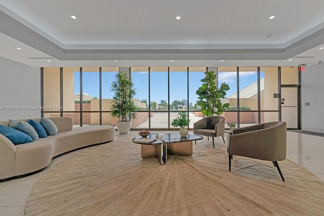 living room with a raised ceiling, light hardwood / wood-style flooring, and a wall of windows