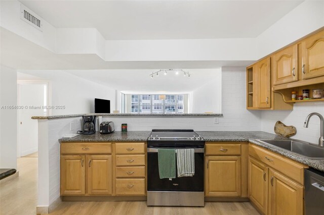 kitchen with dark stone counters, stainless steel appliances, sink, and light hardwood / wood-style floors