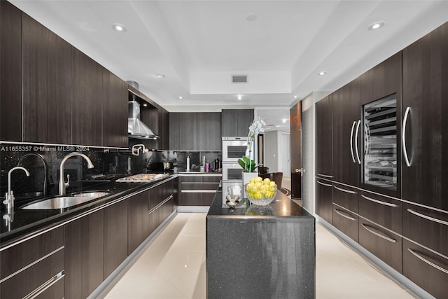 kitchen featuring a tray ceiling, tasteful backsplash, sink, stainless steel gas stovetop, and wall chimney exhaust hood