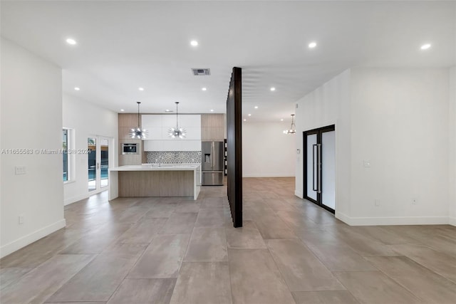 kitchen featuring an inviting chandelier, decorative light fixtures, stainless steel refrigerator with ice dispenser, a kitchen island, and tasteful backsplash